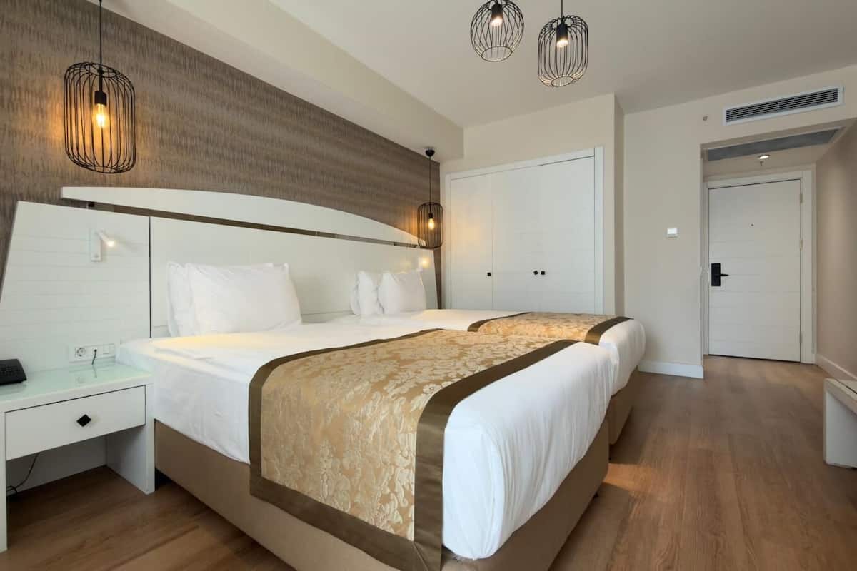 Quarto de hotel com cama, mesa de cabeceira, abajur e guarda-roupa.