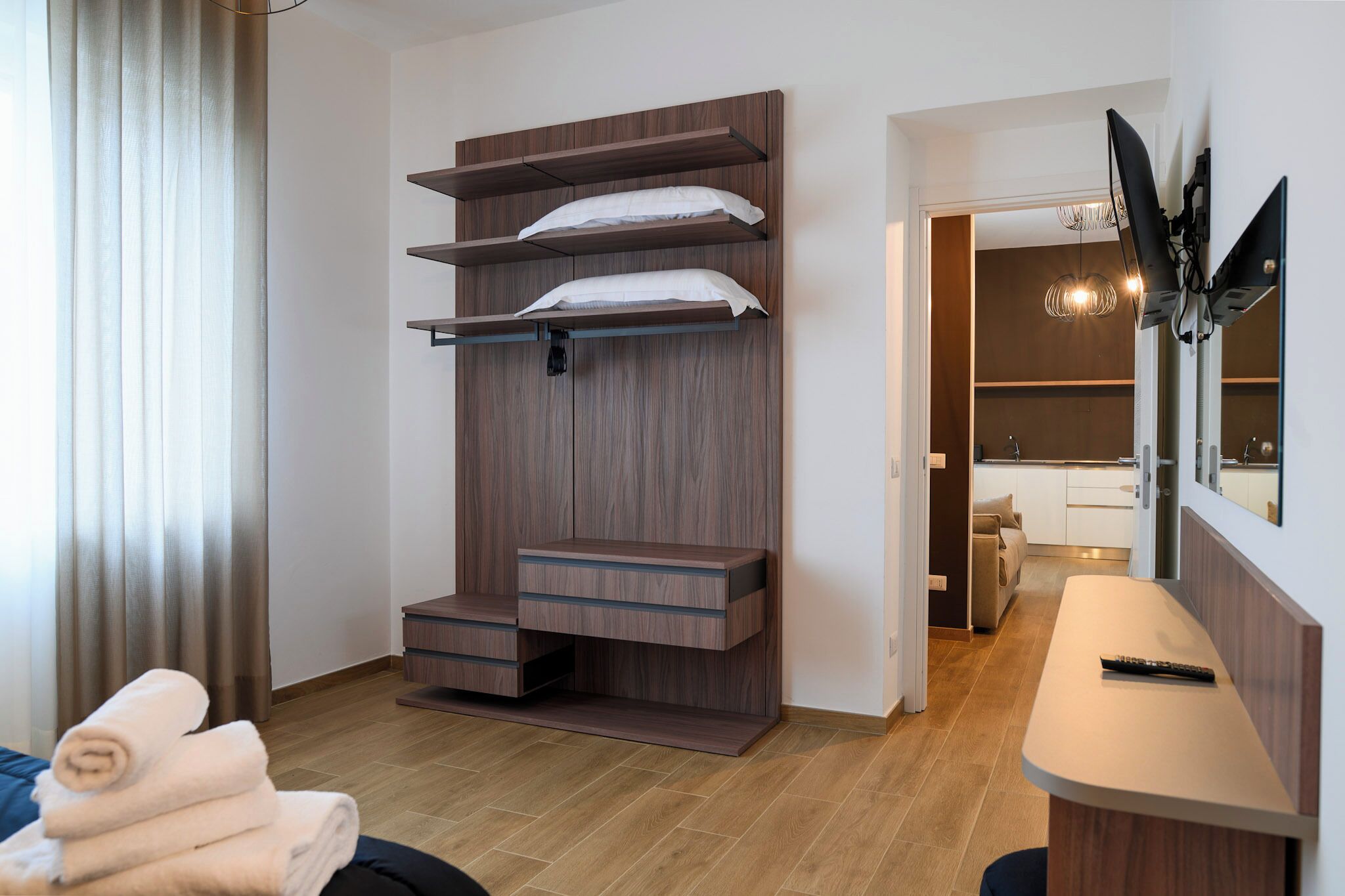 A modern hotel room with a built-in wardrobe, a flat-screen TV, and a small seating area.