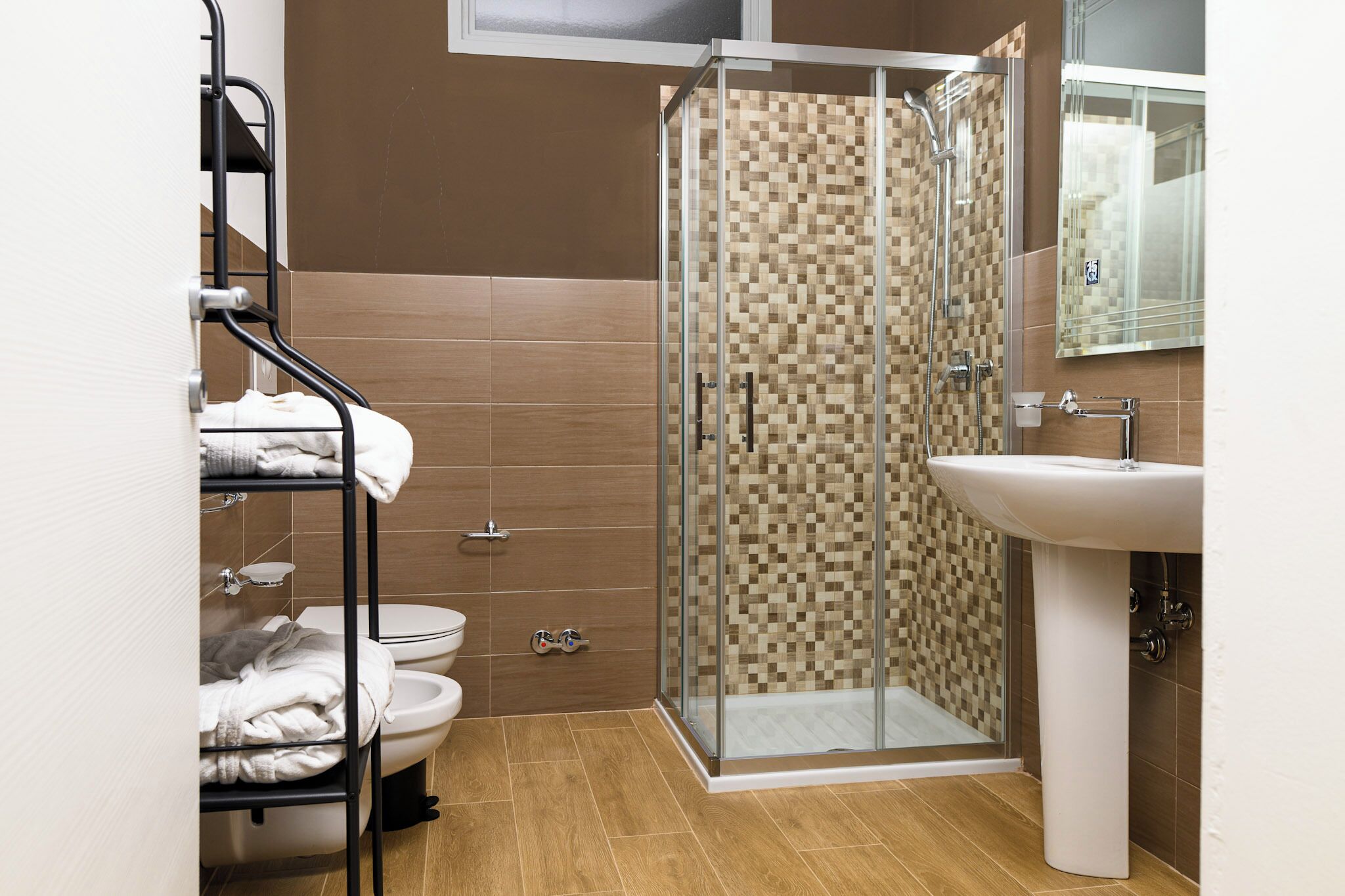 A bathroom with a glass-enclosed shower, a white sink, and a towel rack with folded towels.