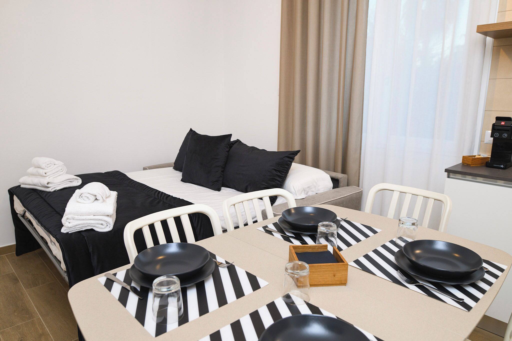 Een hotelkamer met een bed, een eettafel met zwarte borden en bestek, en een koffieapparaat.