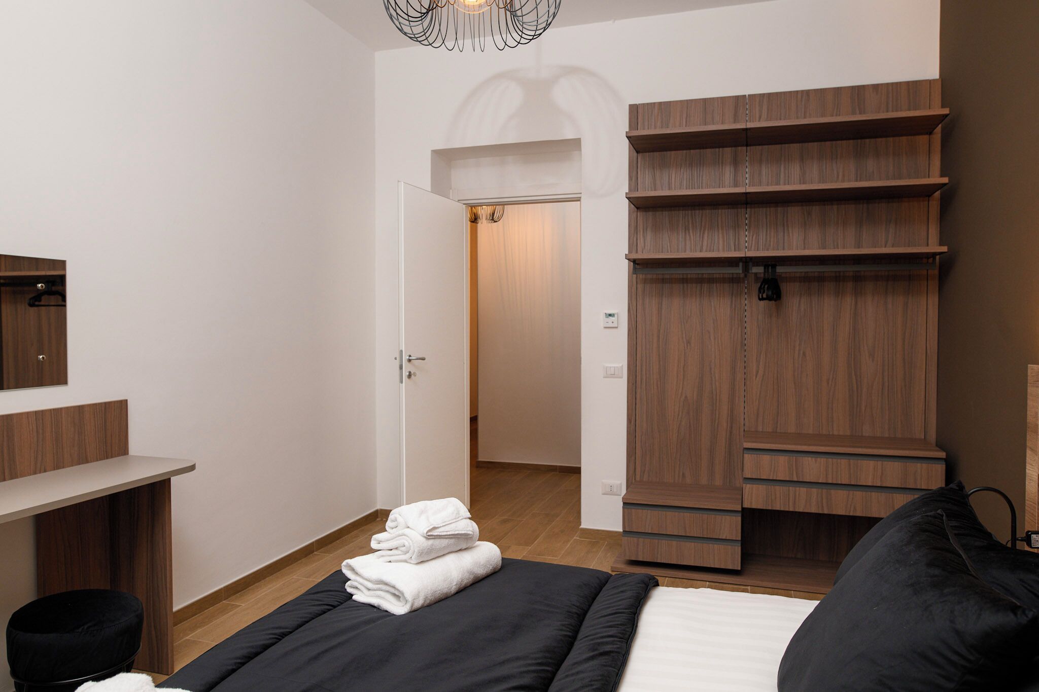 A modern bedroom with a bed, a wooden wardrobe, a desk, and a mirror.