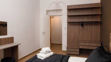 A modern bedroom with a bed, a wooden wardrobe, a desk, and a mirror.