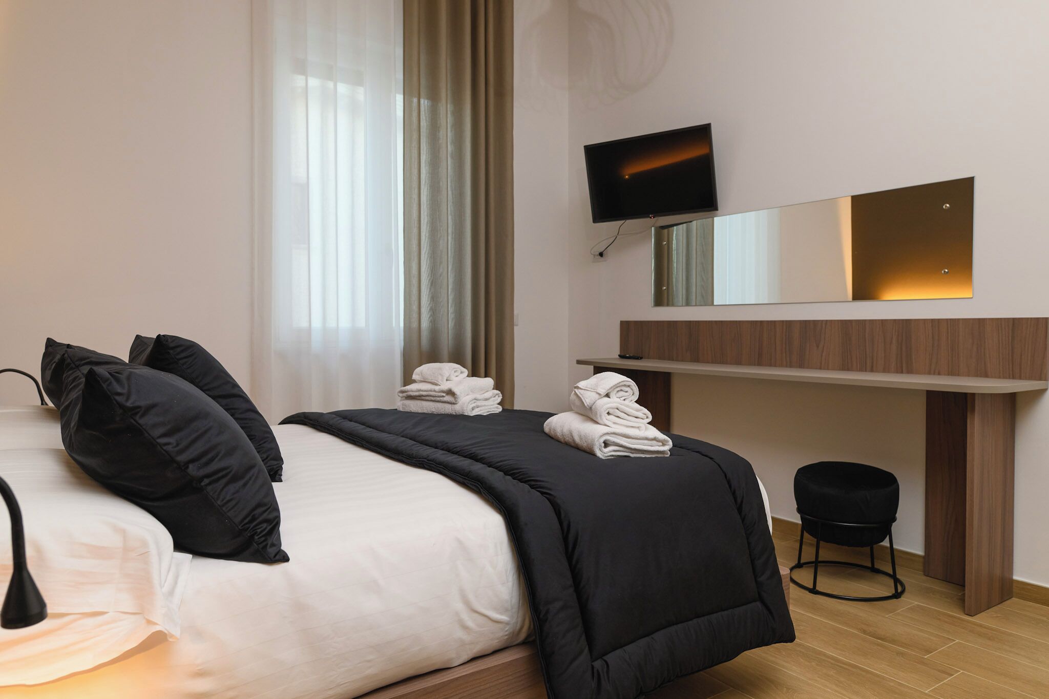 Ett modernt hotellrum med en säng, ett skrivbord, en TV och en spegel.