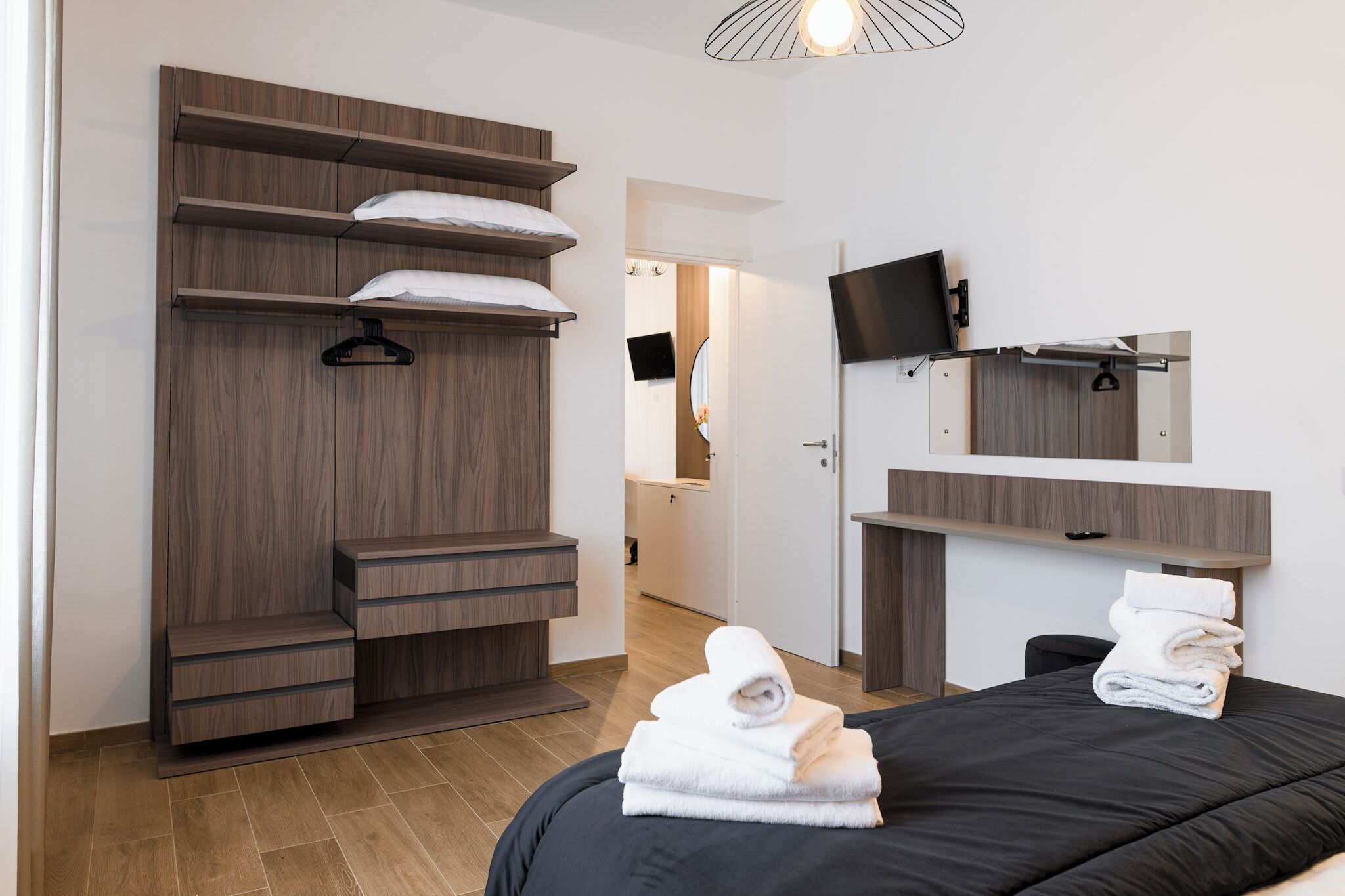 Una habitación de hotel moderna con un armario de madera, una cama con colcha negra y un televisor de pantalla plana montado en la pared.