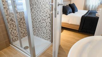 Une salle de bain moderne avec une douche en verre, un plancher en bois et un lit avec une couvre-lit et des oreillers noirs.