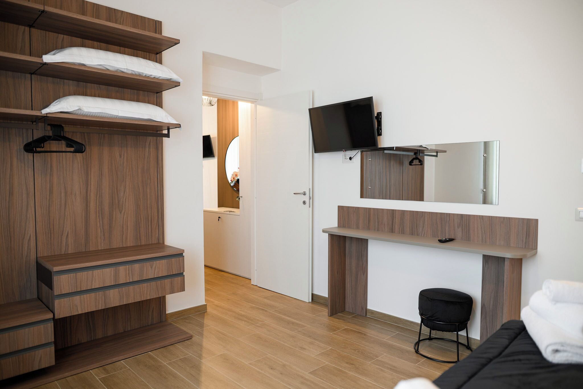 Une chambre à coucher moderne avec une armoire en bois, un téléviseur à écran plat, une coiffeuse avec un miroir et un petit tabouret.