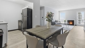 Eine moderne Küche mit integriertem Kühlschrank und Herd, ein Essbereich mit Holztisch und Stühlen sowie ein Wohnzimmer mit Kamin.