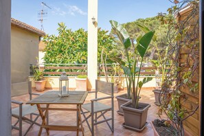Une terrasse extérieure avec une table et des chaises, entourée de plantes en pot et d’une clôture en bois.