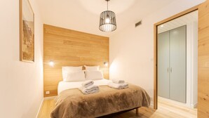 Ein Schlafzimmer mit hölzernem Kopfteil, einem Bett mit weißen Leinentüchern, einer braunen Decke und zwei aufgerollten Handtüchern. Es gibt einen Holzschrank und eine Tür mit satinierten Glasscheiben.