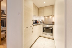 Een compacte keuken met lichte houten kastjes, een roestvrijstalen oven en een aanrecht met keukengerei.