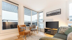 Ein geräumiges Wohnzimmer mit großem Fenster, einem Flachbildfernseher und einer gemütlichen Sitzecke.