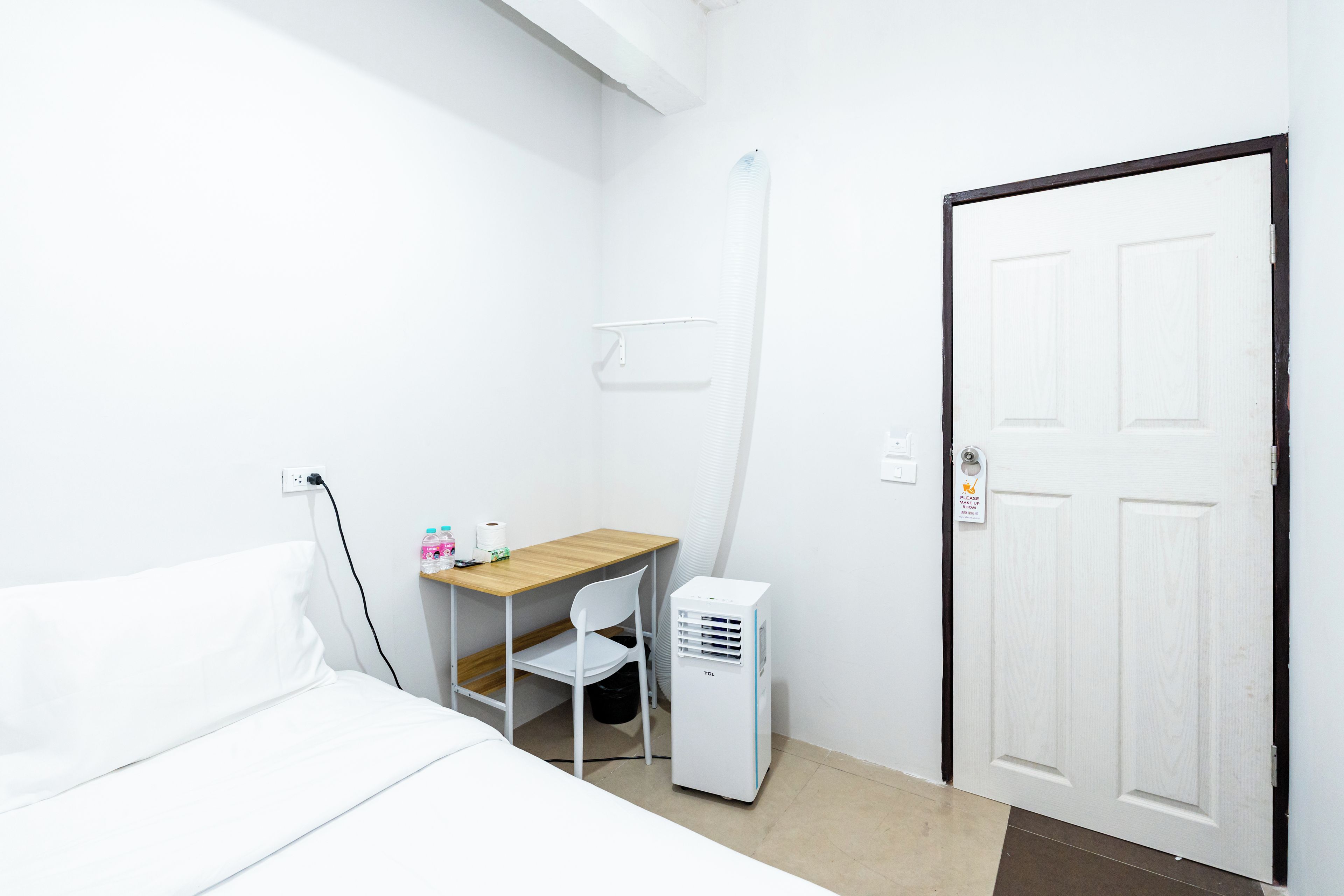 Quarto de hotel com uma cama, uma mesa, uma cadeira, um ar condicionado branco e uma porta.