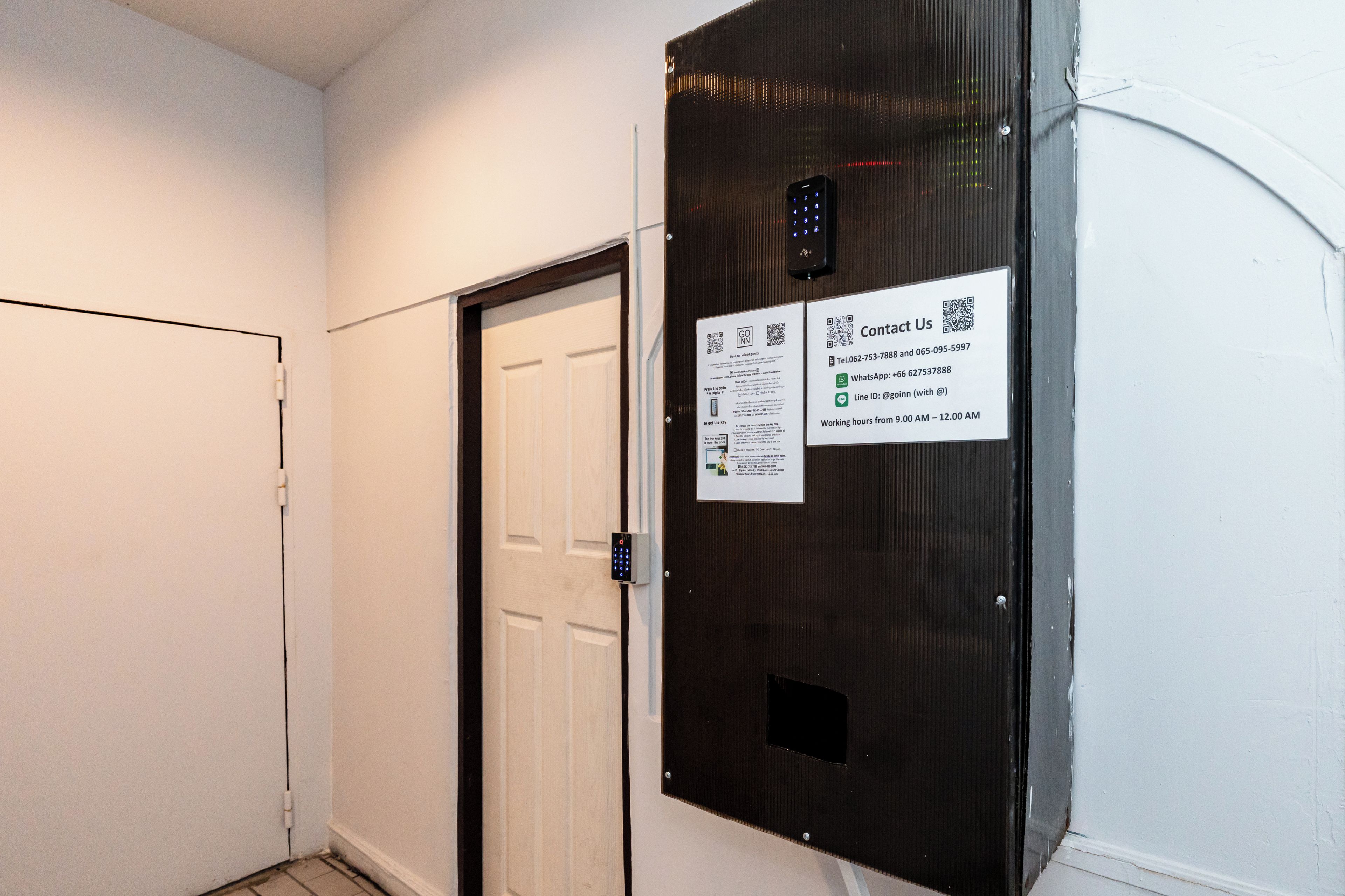 Corredor com porta e painel eletrônico fixado na parede, com aviso de informações de contato.