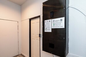 A hallway with a door and a wall-mounted electronic keypad with a contact information sign. - The Hidden Khaosan (Bangkok)