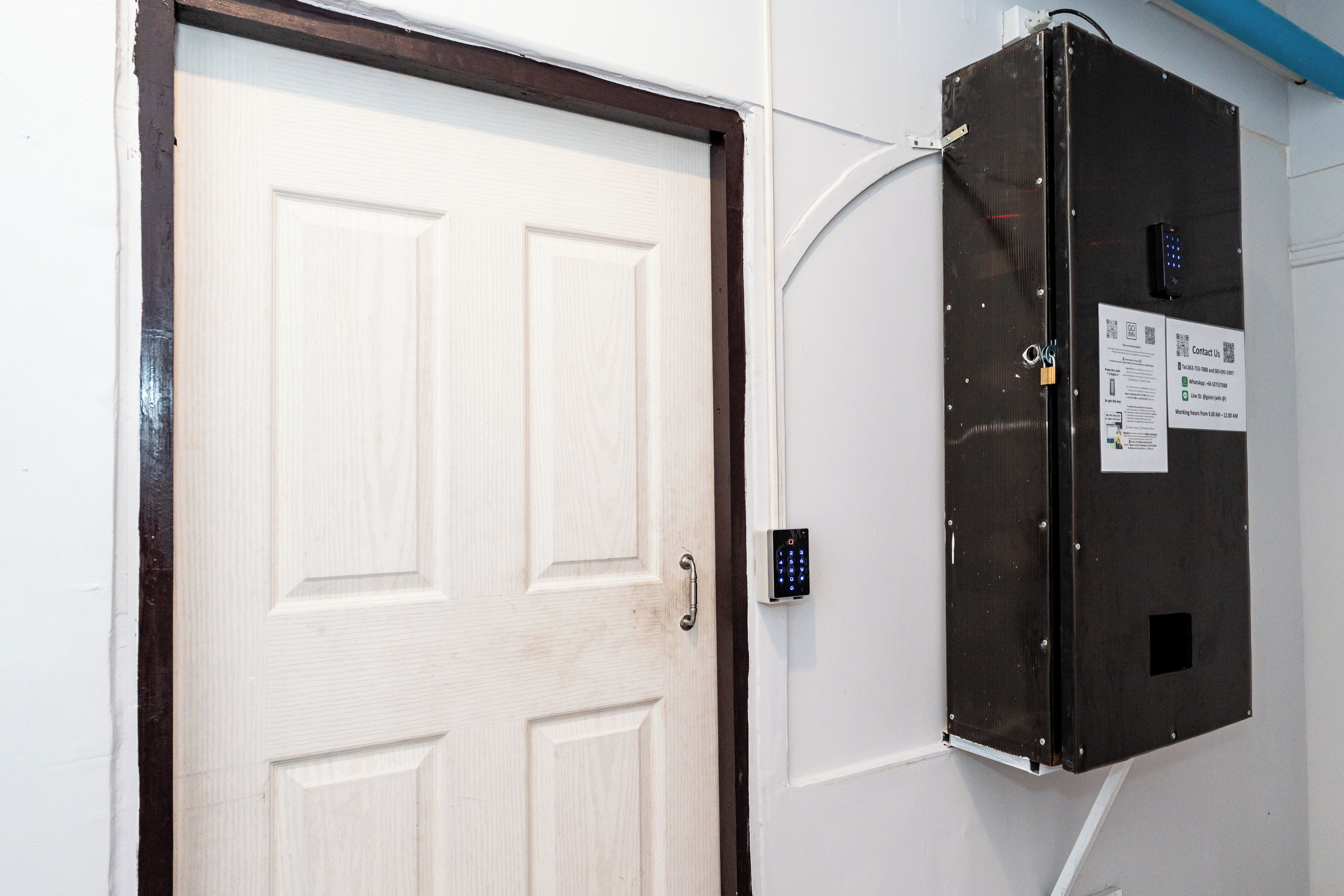 Uma porta com fechadura eletrônica e um aviso com informações de contato na parede.