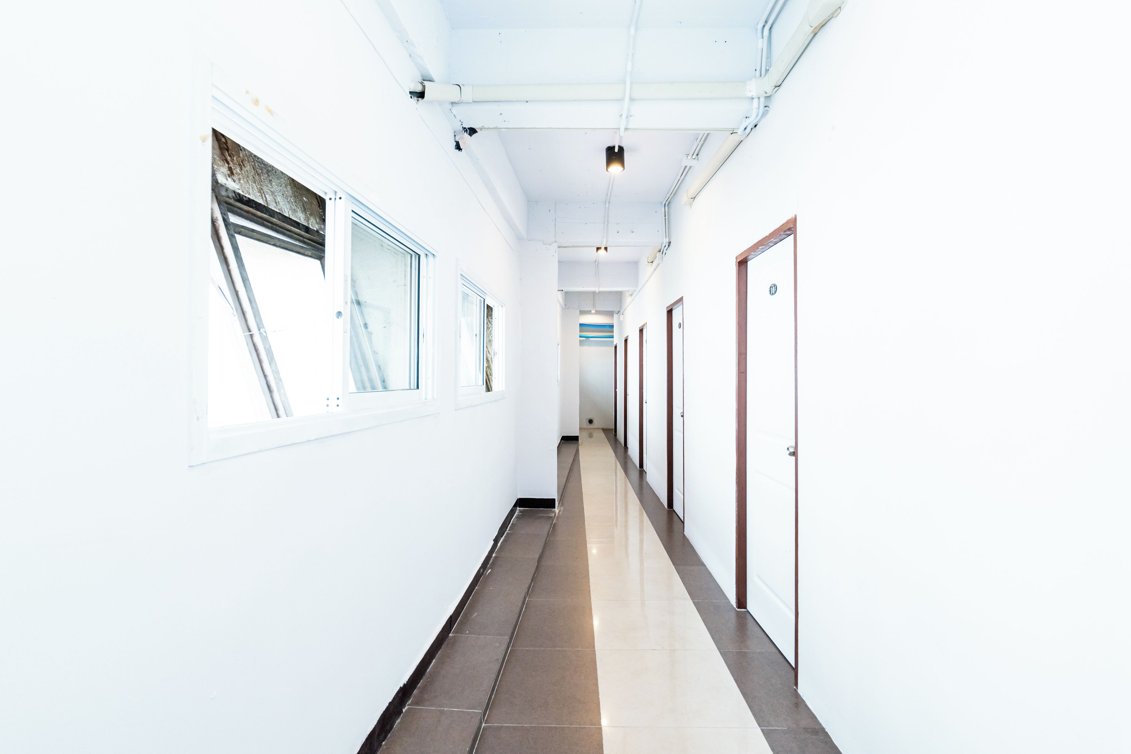 A corridor with white walls, a tiled floor, and doors on one side.