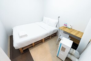 A small, single-bed room with a wooden bed frame, a desk with a chair, a water dispenser, and a toilet. - The Hidden Khaosan (Bangkok)