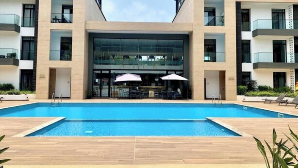 En moderne bygning med en central glasfacade, swimmingpool og udendørs siddepladser.