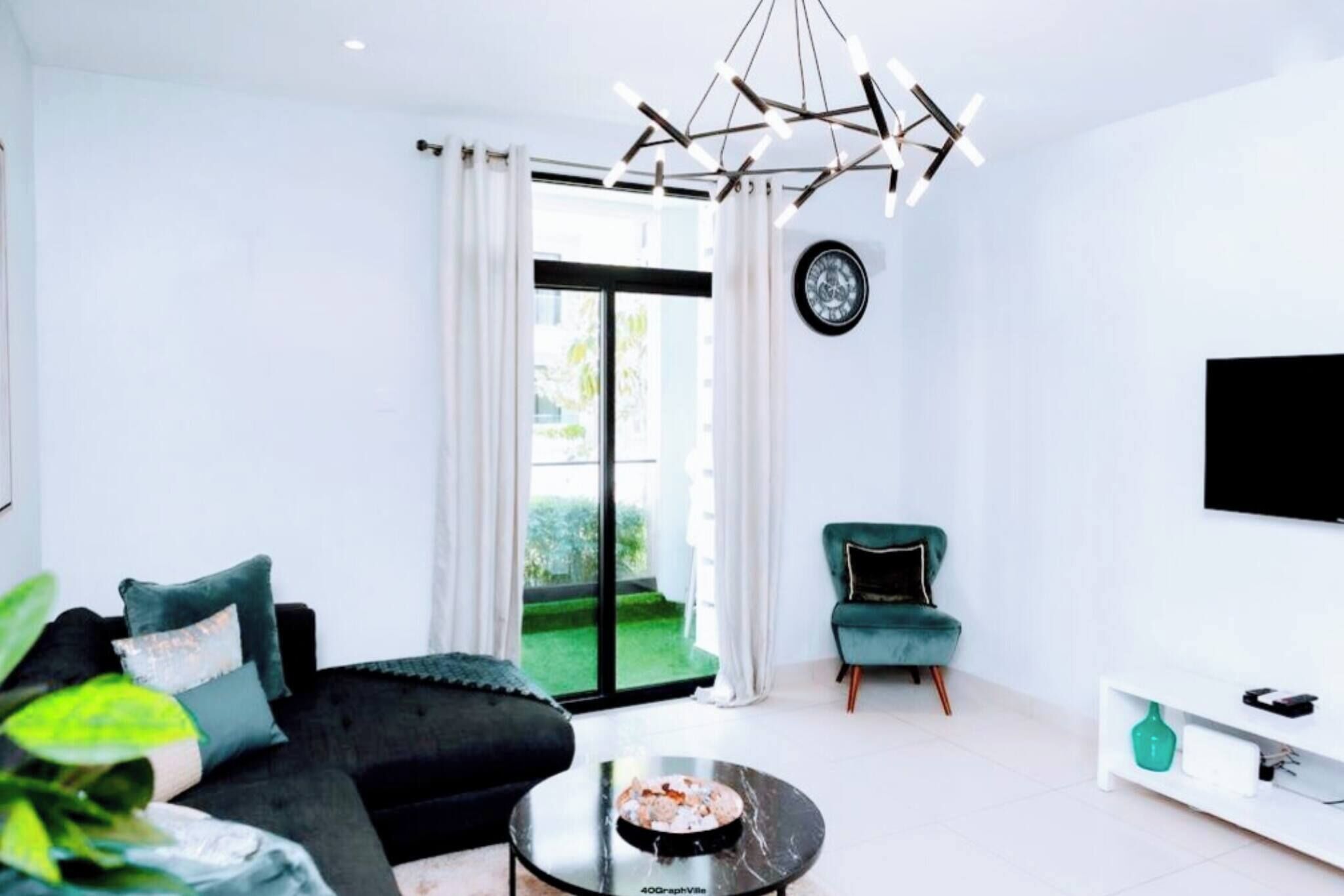 A modern living room with a black sofa, a teal armchair, a coffee table, and a TV mounted on the wall.