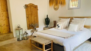 A bedroom with a large bed, wooden headboard, a bench, a cactus, and a hanging light fixture. - HACIENDA LAUTHI (Le Castellet)