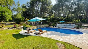 A swimming pool with lounge chairs and umbrellas, surrounded by a stone wall and lush greenery. - HACIENDA LAUTHI (Le Castellet)