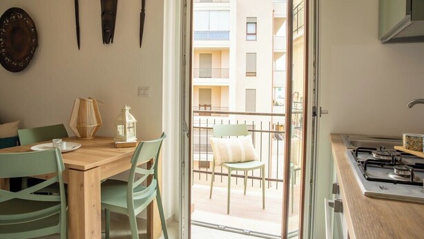 Een keuken met een houten tafel en stoelen, een fornuis en uitzicht op een balkon met een stoel.