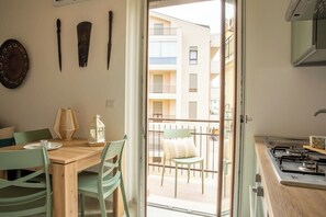 Eine Küche mit Holztisch und -stühlen, einem Herd und Blick auf einen Balkon mit einem Sessel.