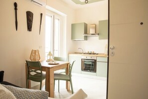 A compact kitchen with a stove, oven, and green cabinets. There is a dining area with a table and chairs, and a window providing natural light. - Apartments The Three Moons-New Moon (Alghero)