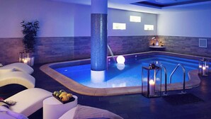 A modern indoor pool area with a blue-tiled column, lounge chairs, and a fruit bowl. - Lite Life Panoramic Flat by Napoliapartments (Naples)