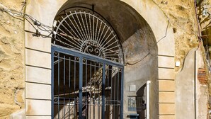 An arched entrance with a metal gate, cobblestone pavement, and a building with a textured wall. - Lite Life Panoramic Flat by Napoliapartments (Naples)