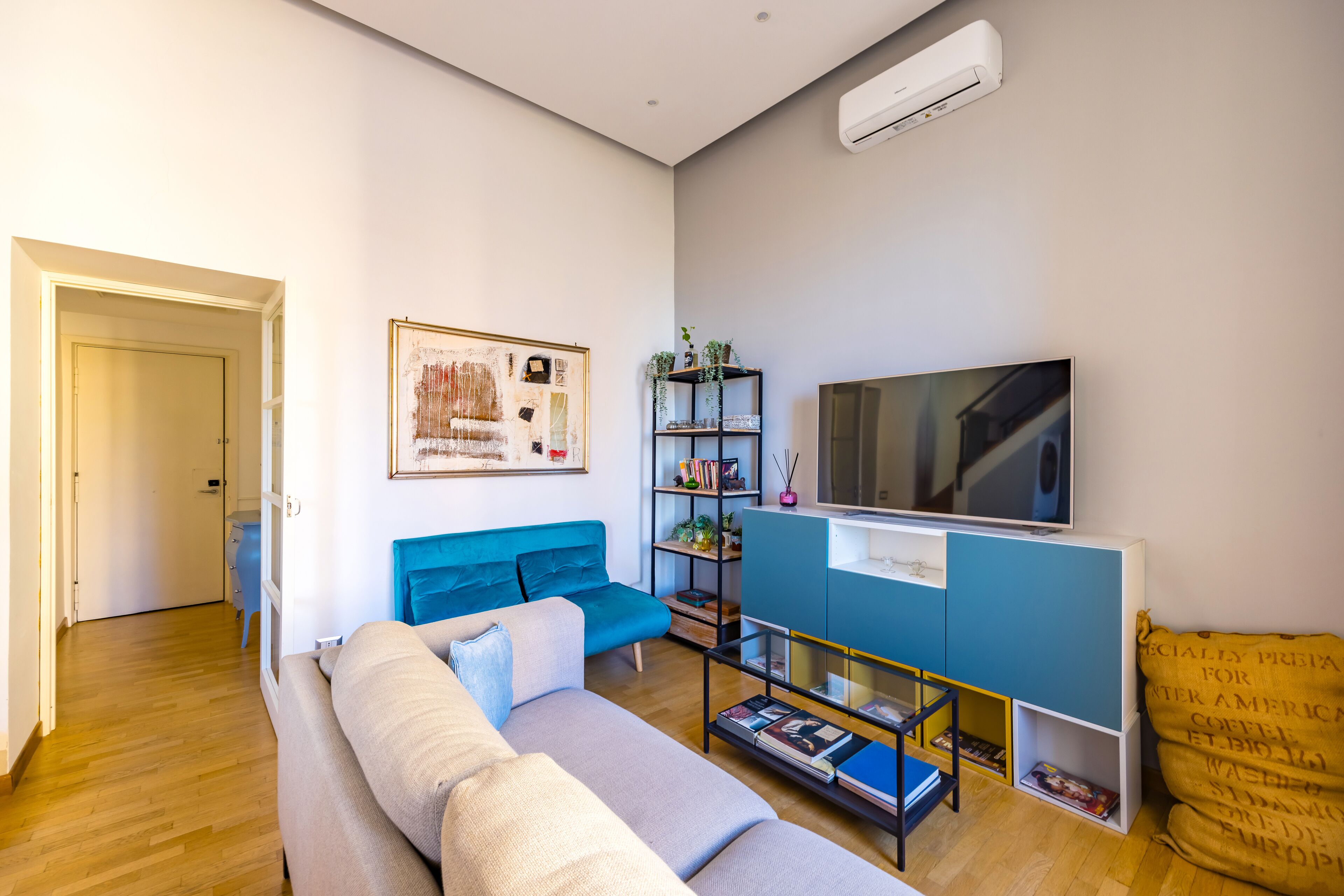 A modern living room with a sofa, a TV, a bookshelf, and a door leading to another room.