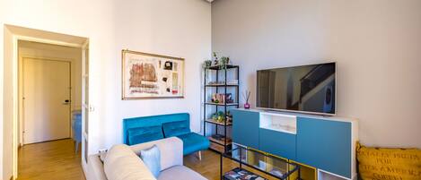 A modern living room with a sofa, a TV, a bookshelf, and a door leading to another room.