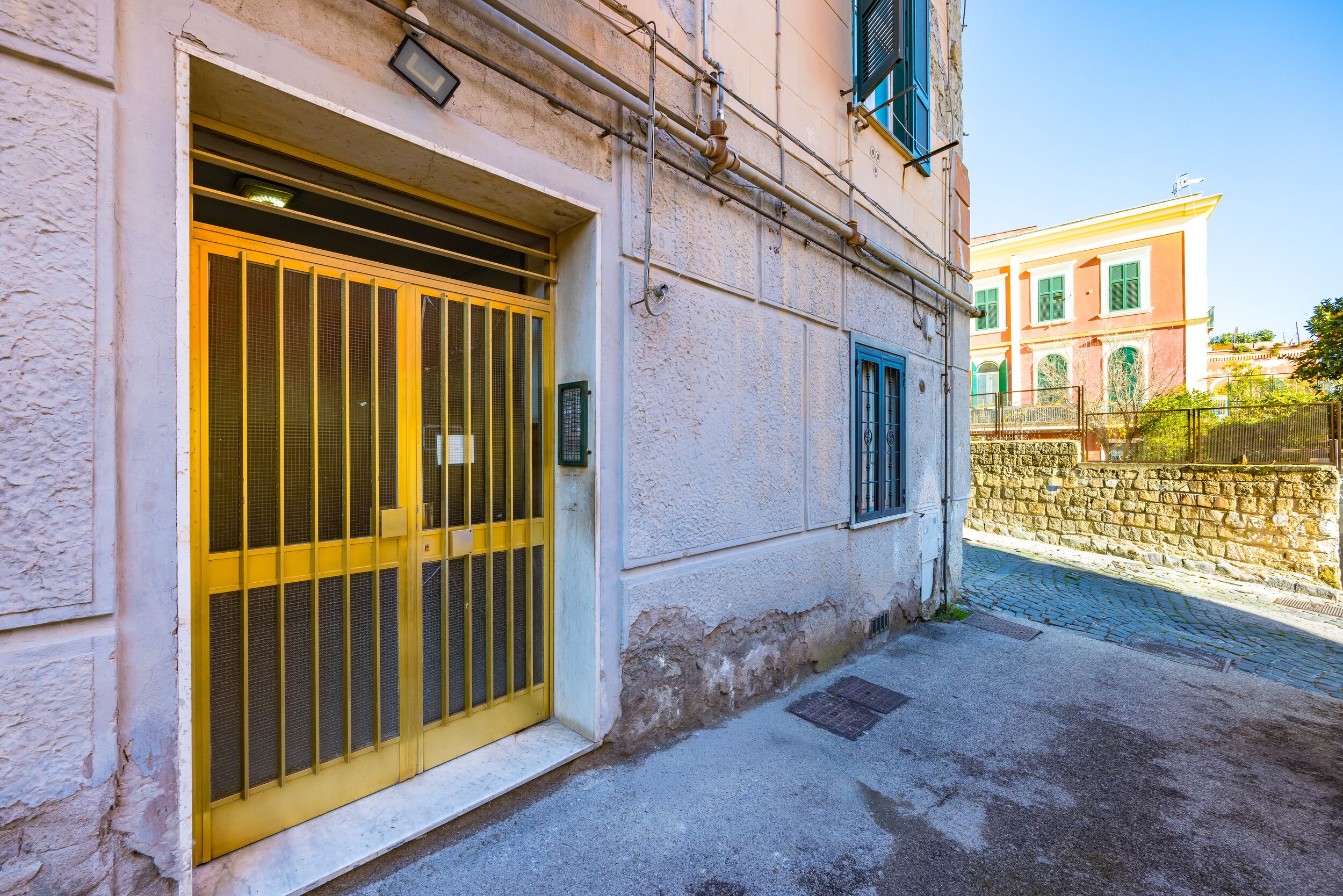 A building with a yellow gate, a stone wall, and a paved street.