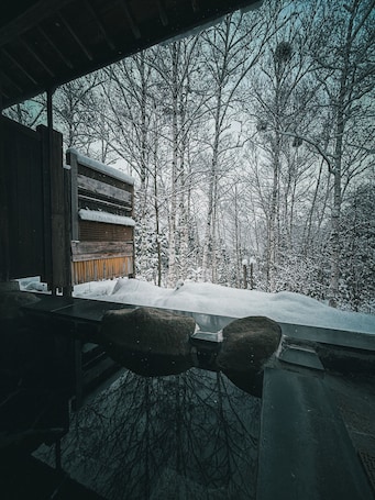 A wooden cabin with a bench and a snow-covered landscape.