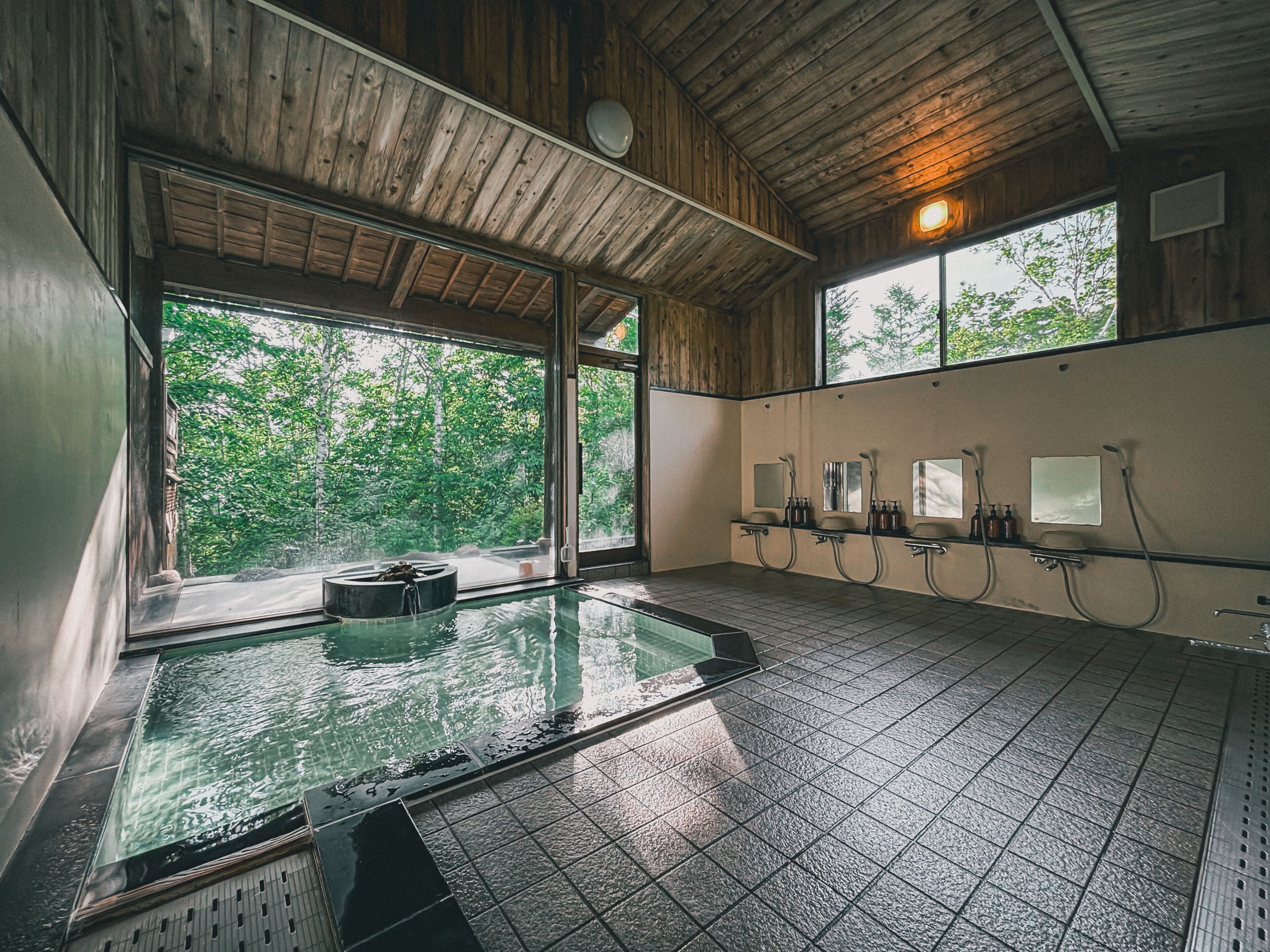 A wooden interior with a large window, a hot tub, and a row of sinks.