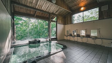 A wooden interior with a large window, a hot tub, and a row of sinks.