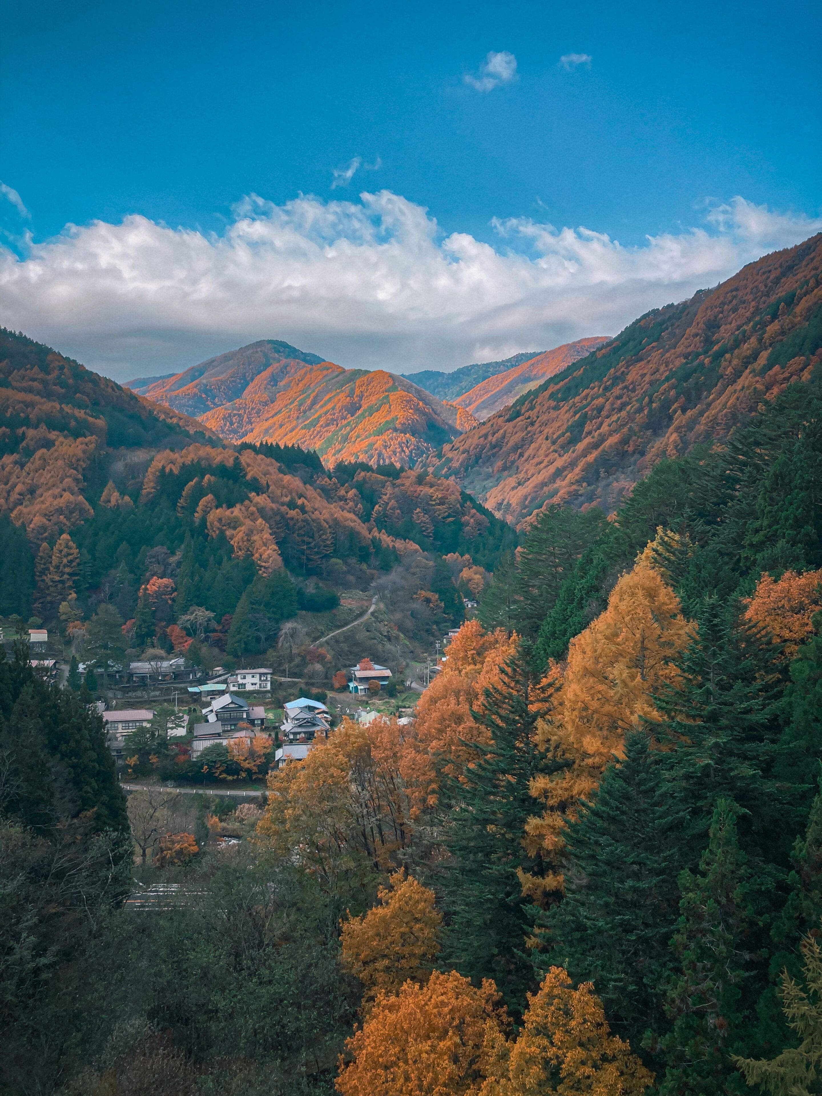 Un paysage montagneux aux couleurs automnales, un petit village avec des maisons traditionnelles et un ciel dégagé.