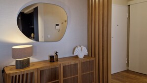 A room with a wooden console table, a round mirror, a lamp, and a decorative shell. - Shell Living - KOS (Funchal)