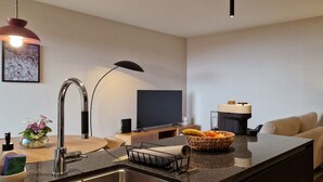 A modern kitchen with a built-in island, a flat-screen TV, a coffee machine, and a bowl of fruit. - Shell Living - KOS (Funchal)
