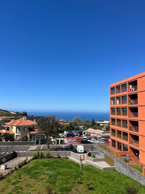 Un quartier résidentiel situé sur la côte, avec un imposant bâtiment orange doté de nombreux balcons, un ciel d’un bleu éclatant et une vue sur la mer.