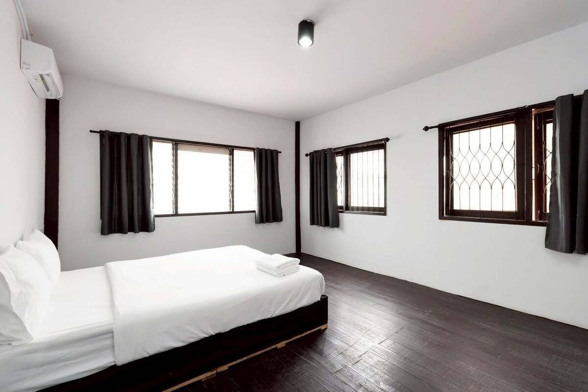 A hotel room with a single bed, two windows with curtains, and a wooden floor.