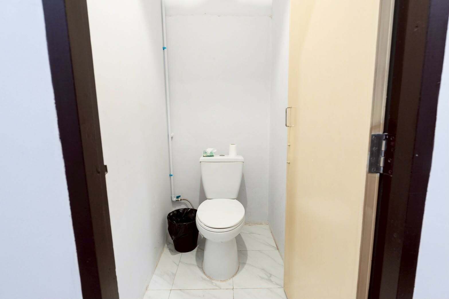 Un bagno piccolo e stretto con un water, un cestino e una parete bianca.