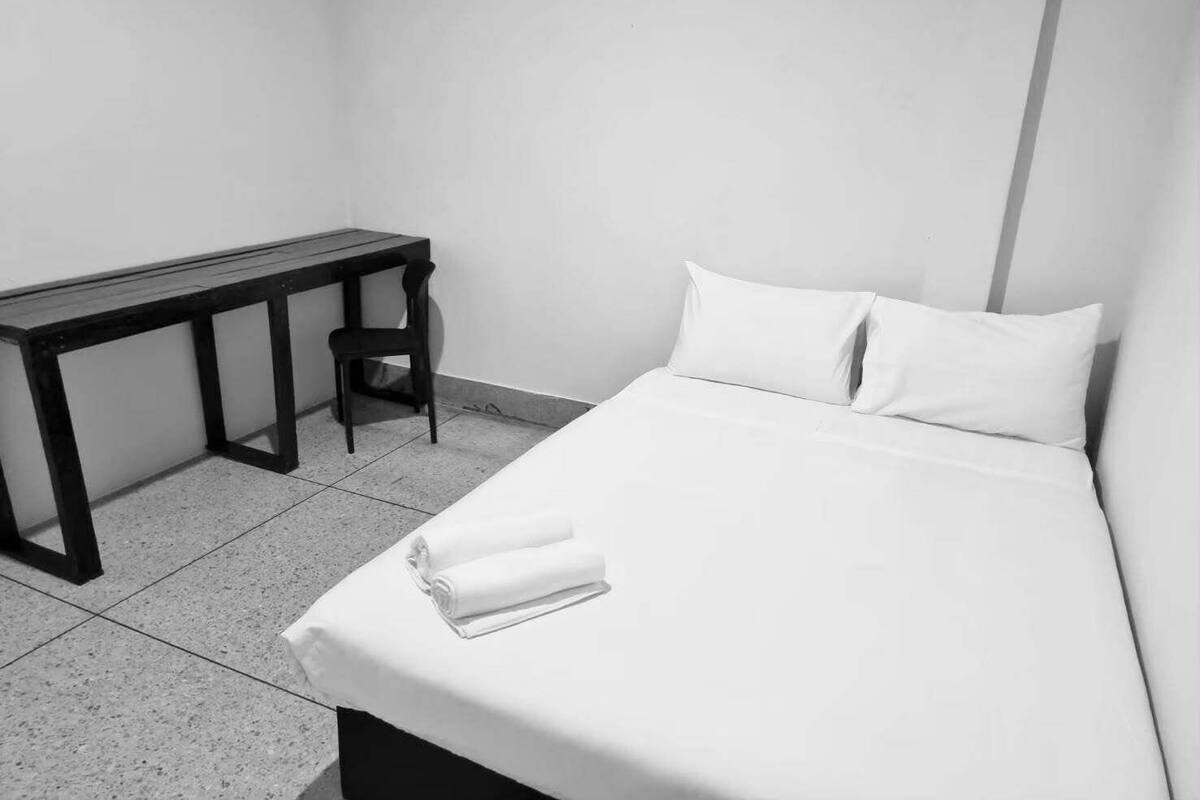 A minimalist hotel room with a single bed, a small desk, and a chair.