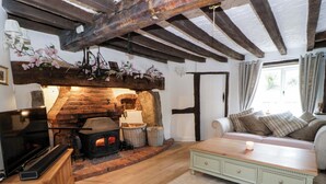 A cozy living room with a stone fireplace, wooden beams, a television, and a sofa with cushions. - The Old Shop (Builth Wells)