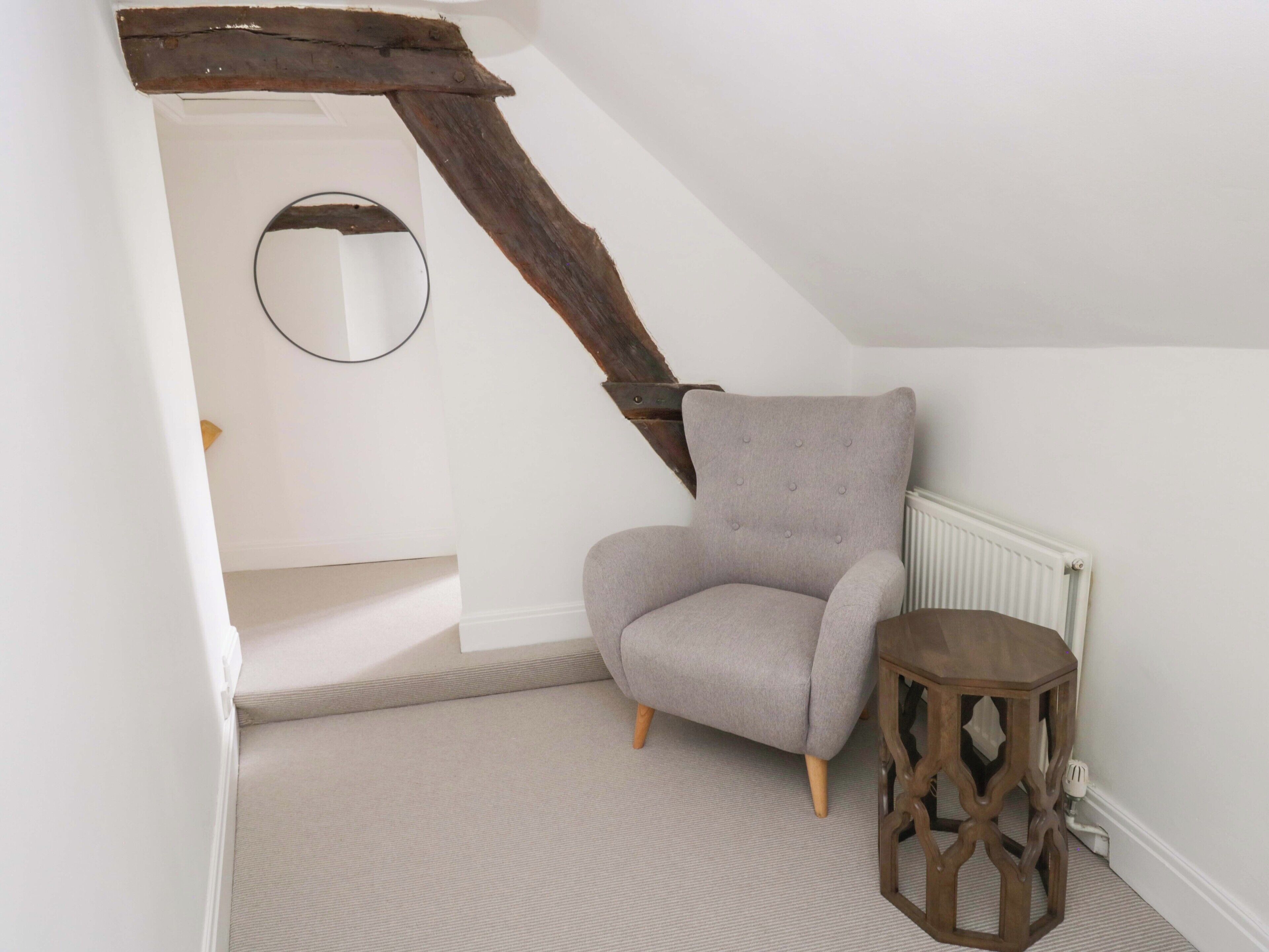 A room with a grey upholstered armchair, a wooden side table, and a white radiator.