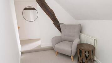 A room with a grey upholstered armchair, a wooden side table, and a white radiator.
