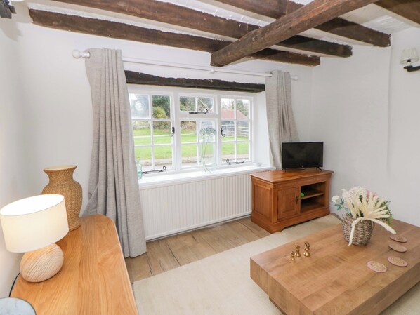 A cozy living room with a wooden TV stand, a lamp, and a chessboard. - The Old Shop (Builth Wells)