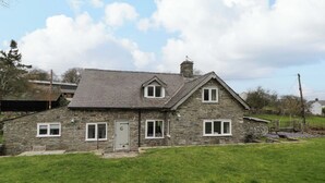A stone house with a grey door, two windows on the upper floor, and a small front porch. - The Old Shop (Builth Wells)