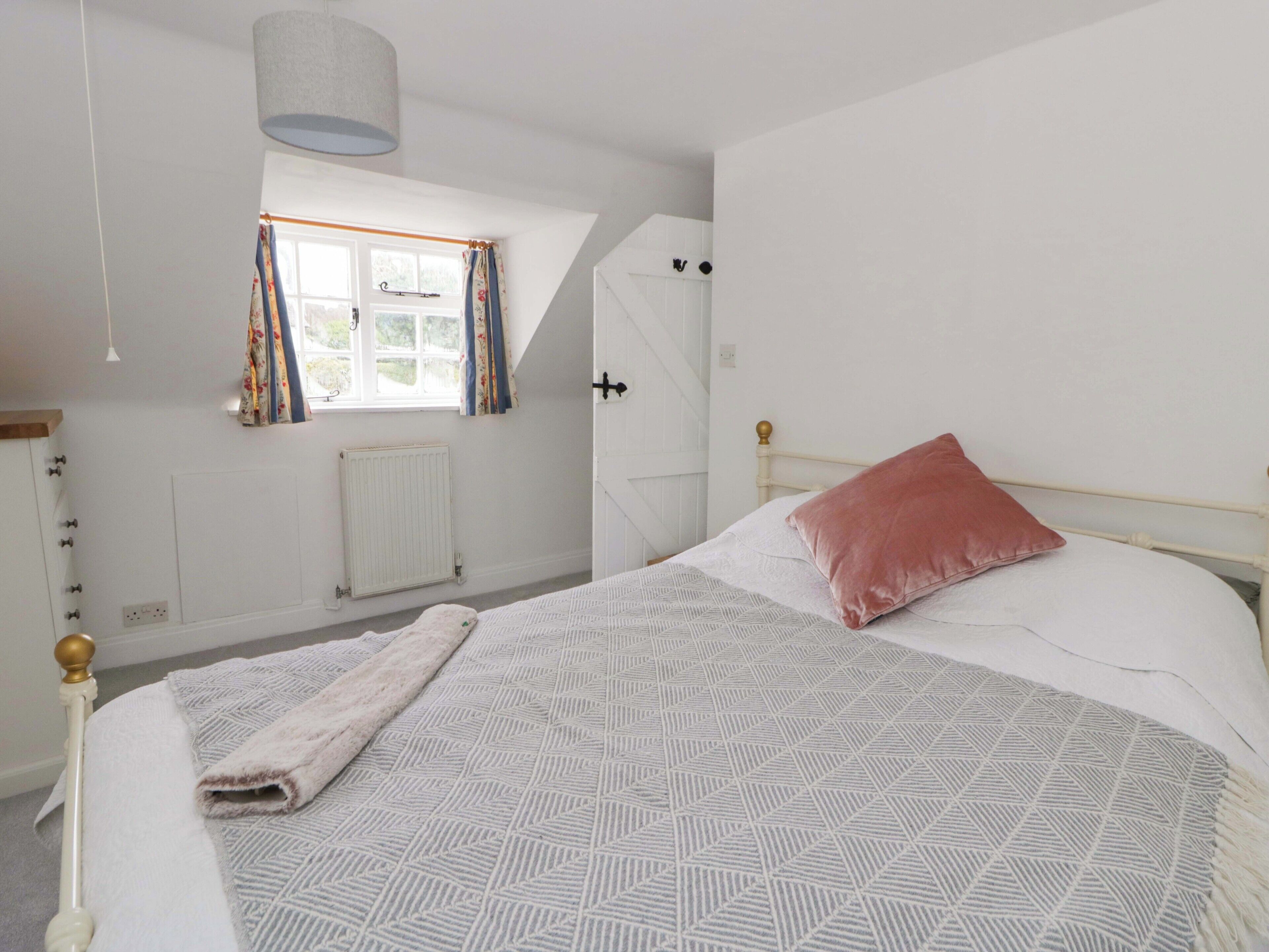 A bedroom with a bed, a window with curtains, a radiator, and a hanging light fixture.