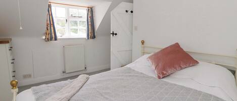 A bedroom with a bed, a window with curtains, a radiator, and a hanging light fixture.